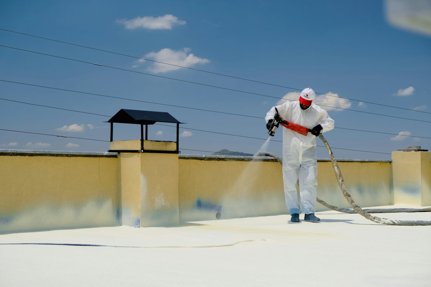 Un technicien pulvérise de l'isolant blanc sur un toit plat.