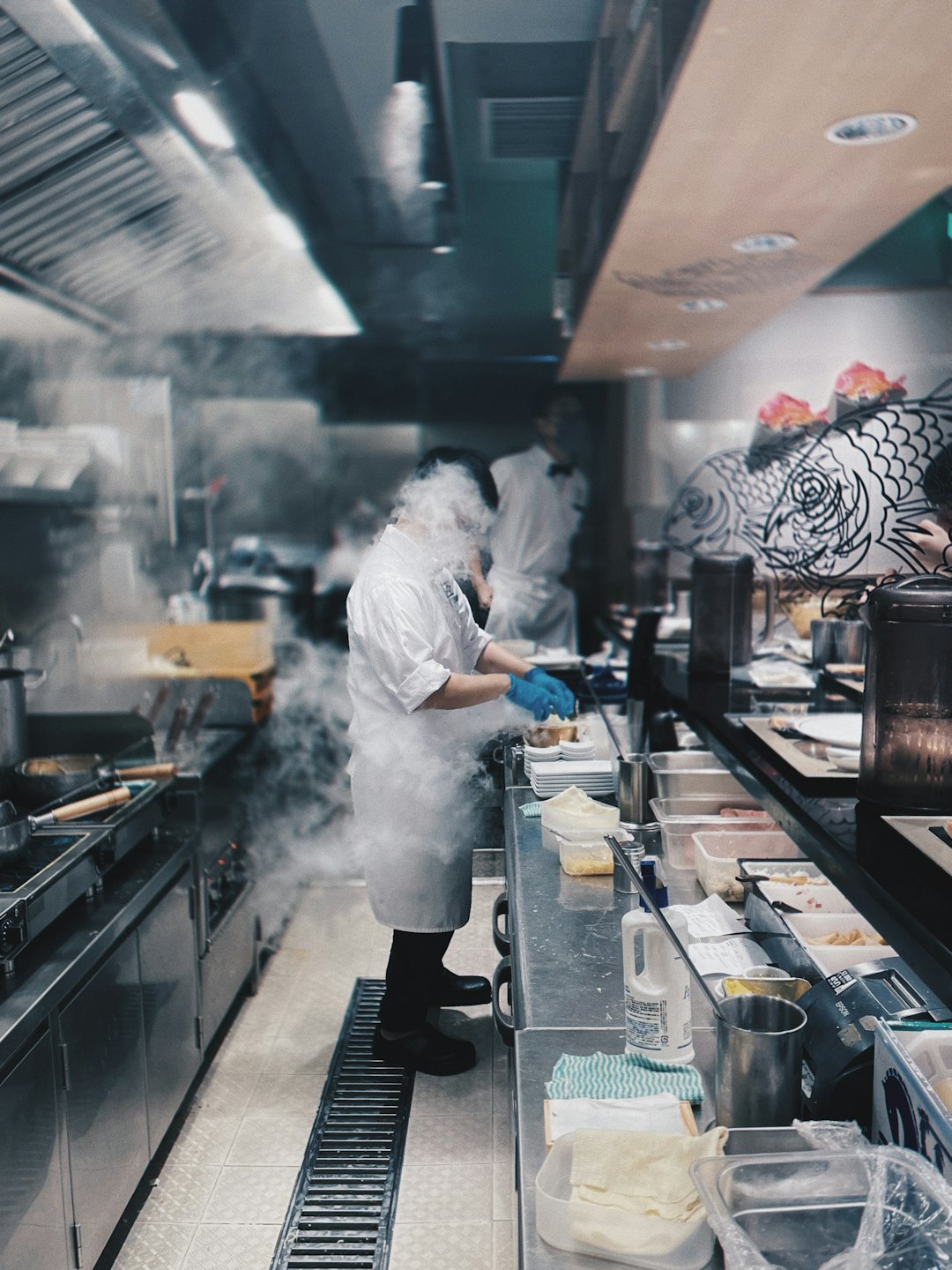 Un chef en gants bleus prépare des aliments sur un comptoir en acier inoxydable.