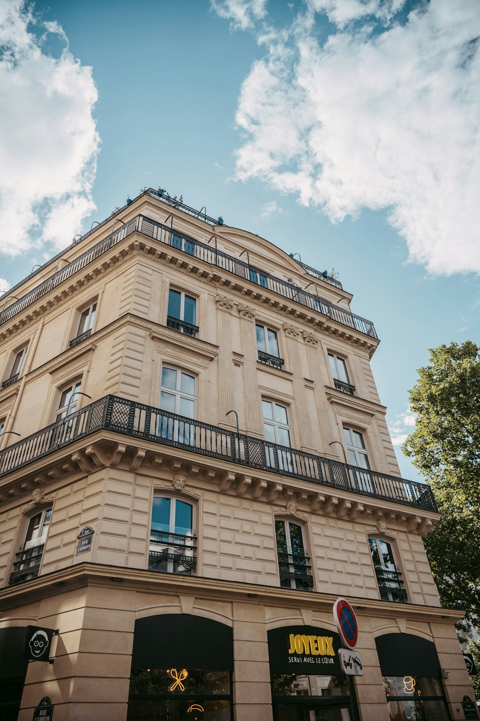 Bâtiment parisien orné avec balcons et boutiques sous un ciel bleu.