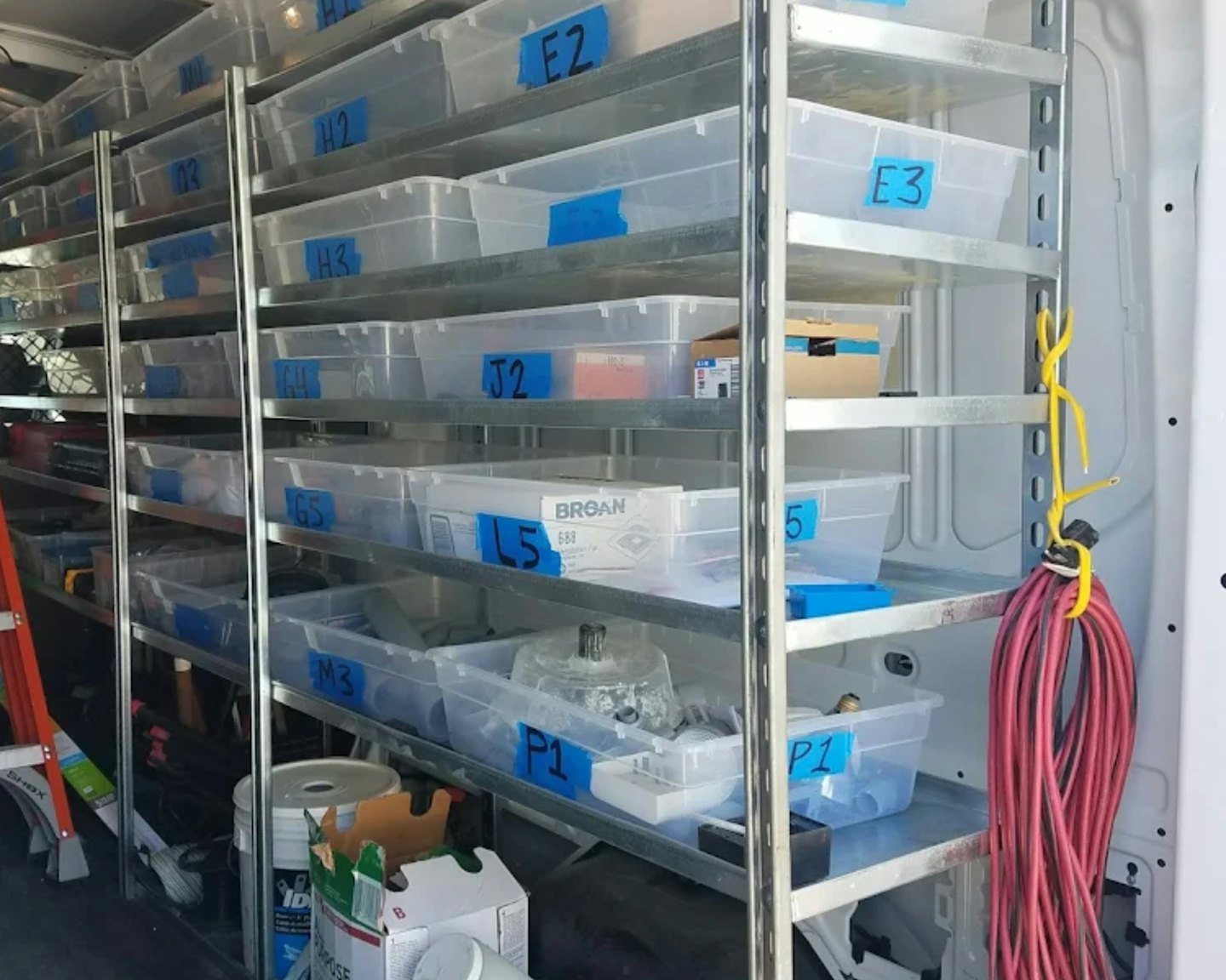 Étagères métalliques organisées avec des bacs étiquetés à l'intérieur d'une camionnette de service.